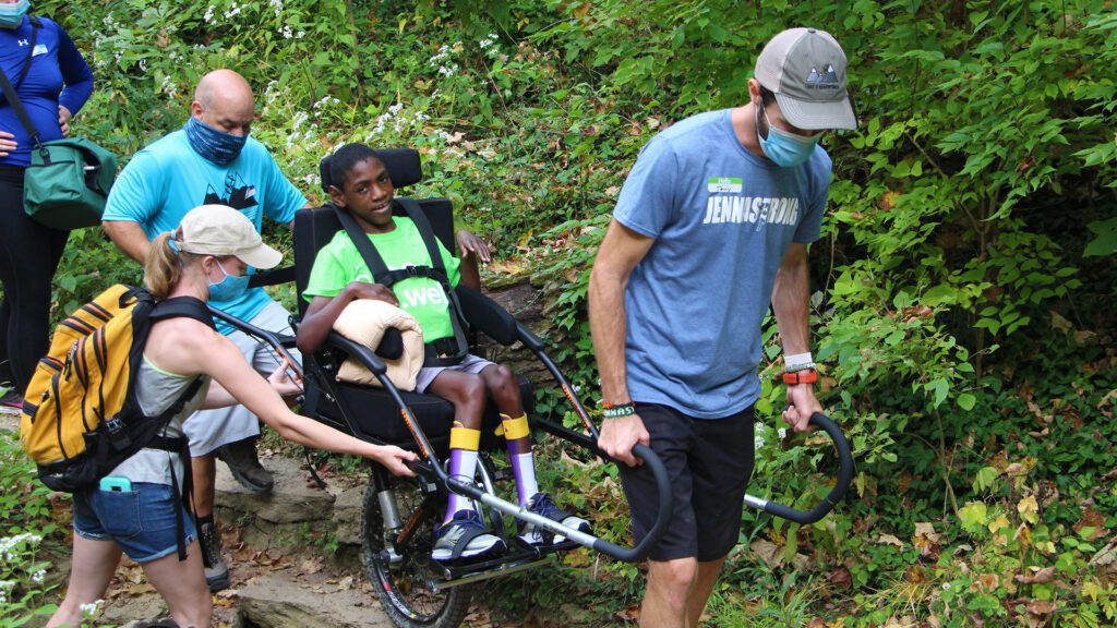 A child being guided through the woods in a special wheelchair
